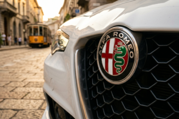 Close-up of an Alfa Romeo car grille with emblem, set on a cobblestone street in a historic city. A vintage yellow tram is blurred in the background.
